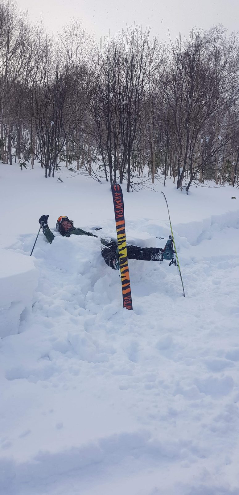 Noah sitting waist-deep in fresh powder snow, skis standing upright beside him